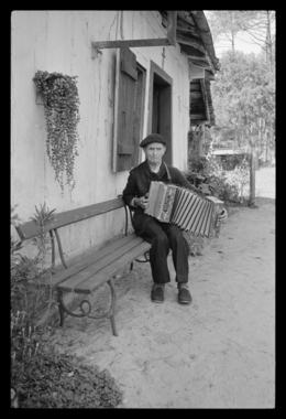 Louis Pinsolle jouant de l'accordéon devant sa maison la vignette