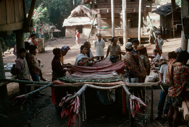 7. Accrochage des tissus au mât cérémoniel., 7. Attaching cloths to the ceremonial mast. (anglais), 7. Pemasangan kain pada bendera seremonial. (indonésien) la vignette